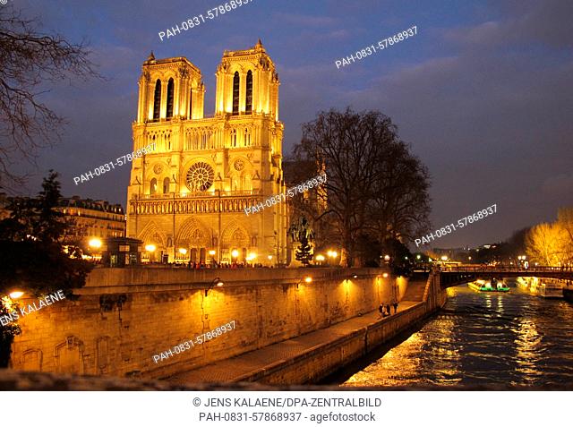 The famous cathedral of Notre-Dame shines illuminated at dusk on the Ile de la Cite, the island in the middle of the River Seine, in central Paris, France