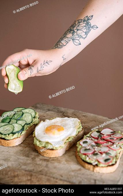 Woman squeezing lime on bread garnished with vegetable and guacamole on serving dish at kitchen