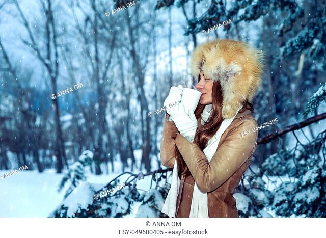 Calm contented woman gladly drinks hot coffee among snow-covered trees, enjoys the winter holidays walking in the park