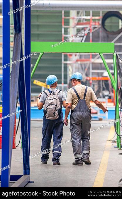 14 July 2021, Mecklenburg-Western Pomerania, Wismar: Two shipbuilders walk along the dock of the MV shipyard. The ship, intended for the Asian market and...