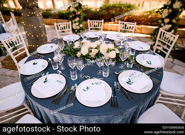 White round plates on a round table with gray tablecloth, white Chiavari chairs with white pillows. A floral arrangement in the center of the table