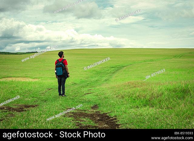View of traveler man on a beautiful road in the countryside. Young explorer man walking in a green field, Backpacker man walking in a beautiful field