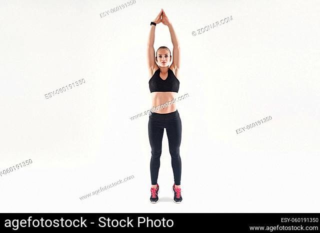 Easy aerobic exercising. Hands up and toe standing. Beautiful blonde woman. Studio shot, isolated on gray background
