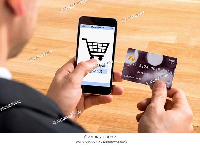 Close-up Of Businessman Holding Credit Card With Mobile Phone Showing Shopping Cart Symbol