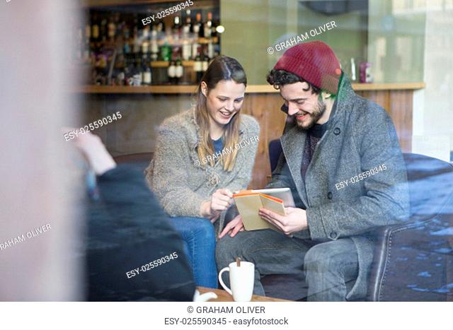 Young man and woman sitting in a cafe looking at a digital tablet together