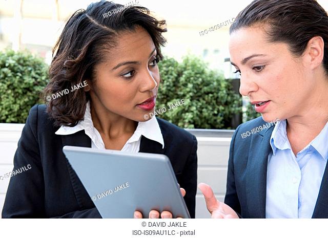 Two businesswomen looking at digital tablet, outdoors