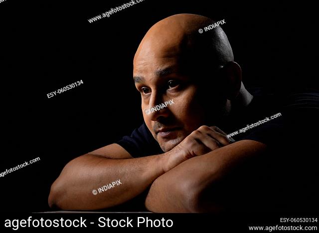 Portrait of a bald man gazing with an anxious look against dark black background