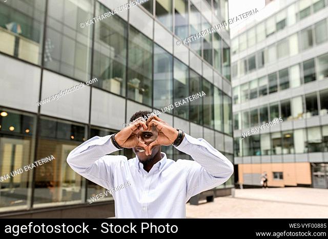 Young man making heart shape in front of building