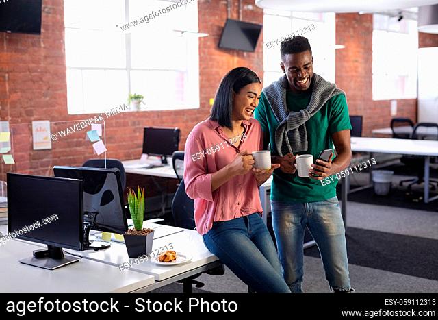 Diverse business colleagues having coffee in office and looking at smartphone