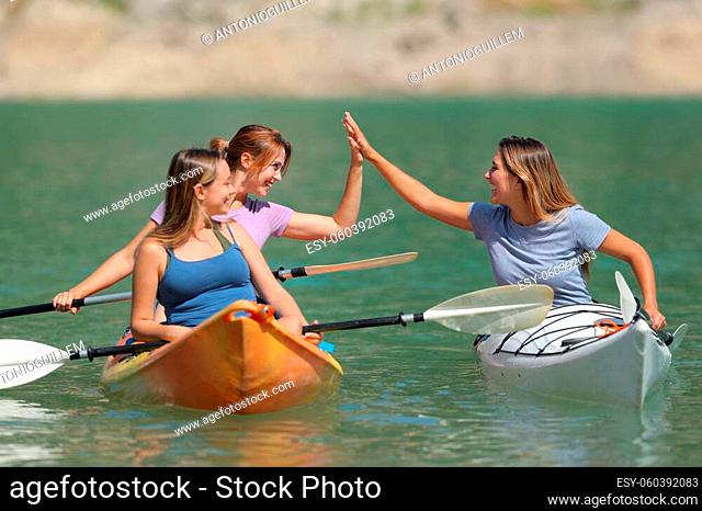 Three friends giving five enjoying a kayak day in a beautiful lake on summer vacation