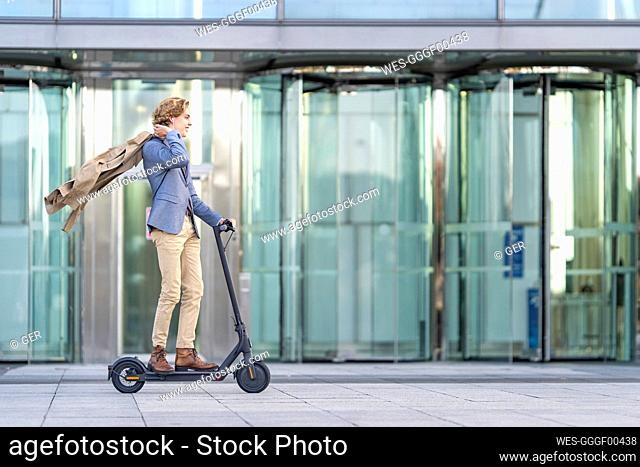 Carefree businessman riding electric push scooter on footpath