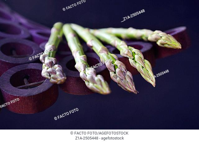 Five green asparagus on a violet holder on dark blue background