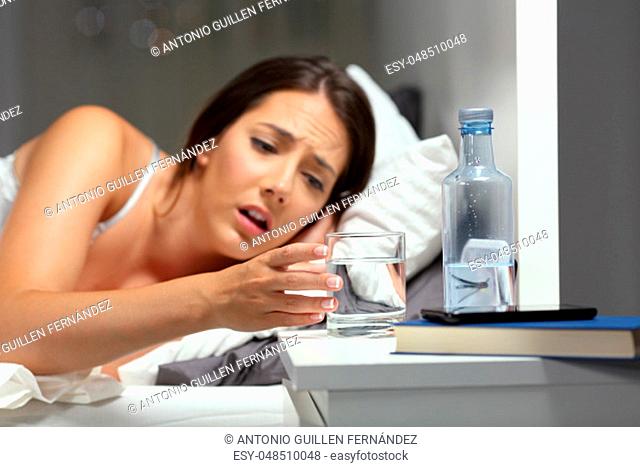 Dehydrated woman reaching a glass of water on the bed in the night at home
