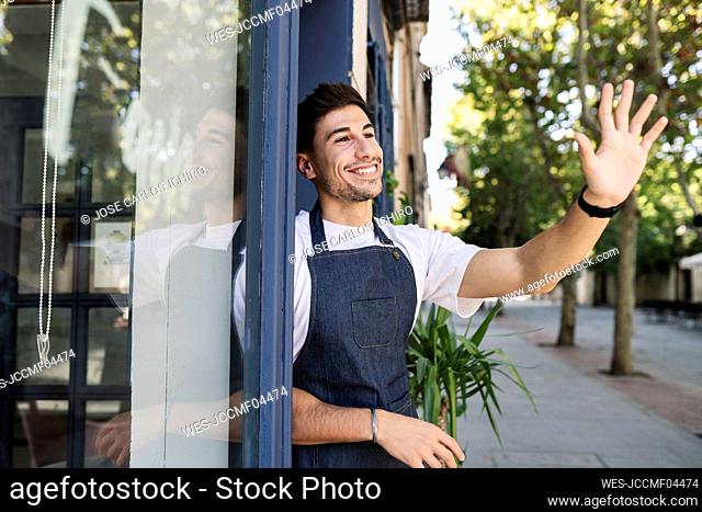 Smiling owner waving hand at cafe entrance