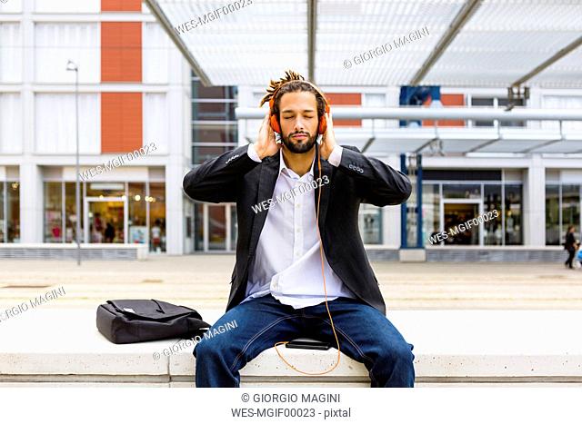 Portrait of young businessman with dreadlocks listening music with headphones and cell phone