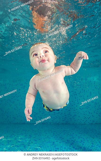 Little baby boy learning to swim underwater in a swimming pool. Healthy family lifestyle and children water sports activity