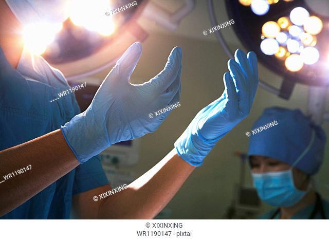 Midsection view of hands in surgical gloves and surgical lights in the operating room