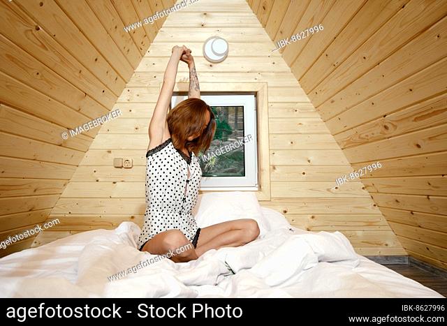 Unrecognizable young woman stretching herself awake in her bed in a-frame house