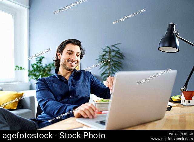 Smiling businessman using laptop at desk while sitting in office