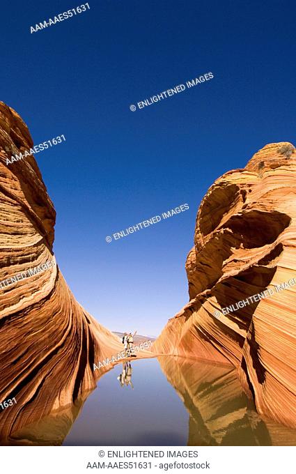 Tourist Couple next to Seasonal Desert Pool of Water below striated Sandstone at The Wave, Coyote Buttes, Paria Canyon Vermilion Cliffs Wilderness w  people