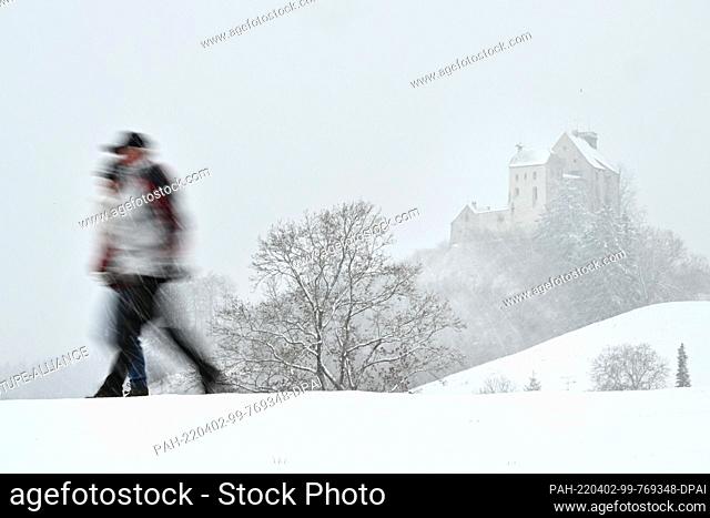 02 April 2022, Baden-Wuerttemberg, Waldburg: A couple walks through the fresh snow, while in the background lies the Waldburg