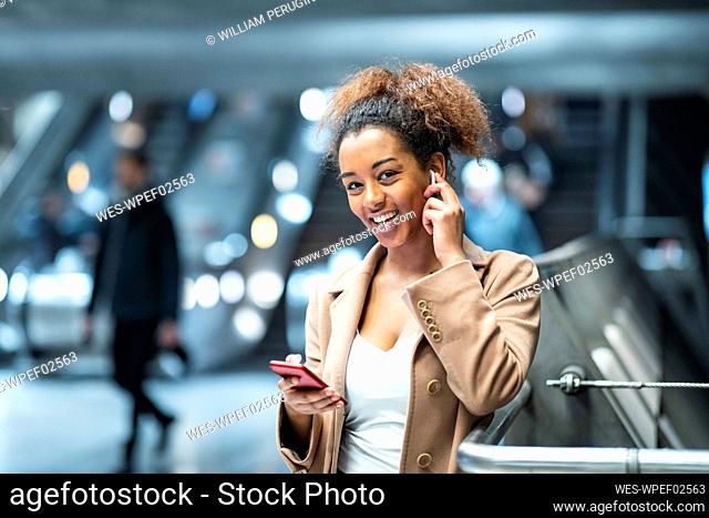 Portrait of happy young woman with cell phone and earbuds at subway station