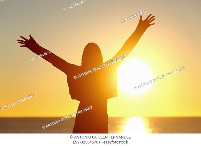 Free happy woman raising arms watching the sun in the background at sunrise
