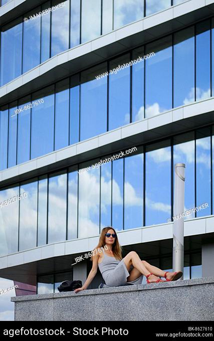 Pretty girl sitting on marble surface with bent knee. Reflection of the sky in windows