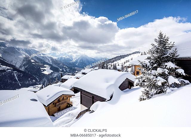 Clouds and blue sky frame the mountain huts covered with snow Bettmeralp district of Raron canton of Valais Switzerland Europe