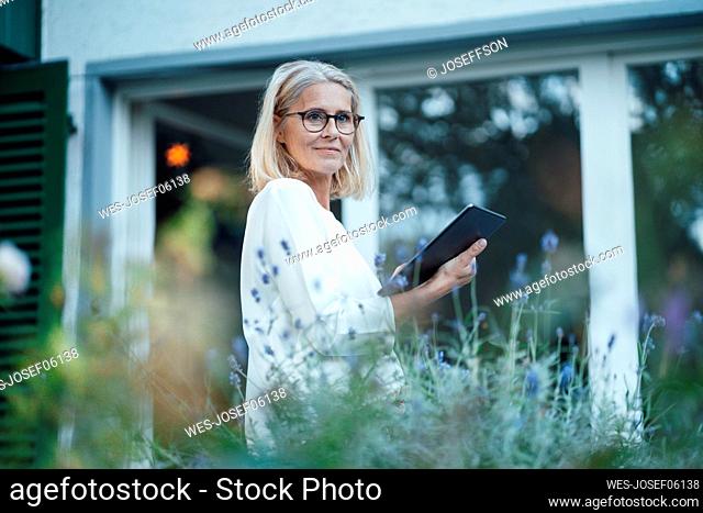 Blond woman with eyeglasses and tablet PC at garden