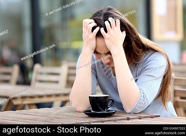 Sad woman complaining alone sitting on a coffee shop terrace