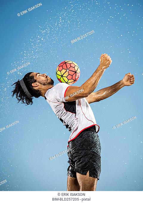 Water spraying on Hispanic man trapping soccer ball on chest