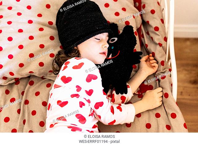 Little girl wearing cap sleeping in bed with her soft toy