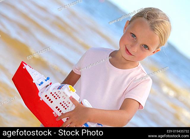 little blonde girl playing with a boat near the sea