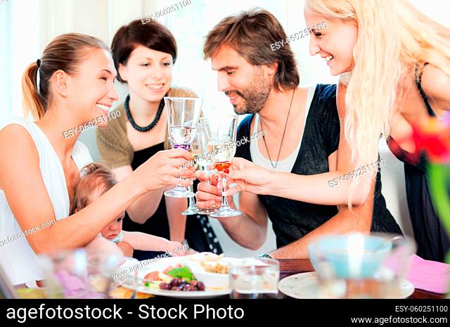Four young people and a baby are celebrating in restaurant in casual clothing. Focus on glasses