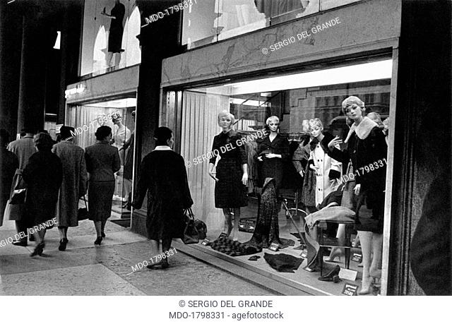 Women having a stroll catch a glimpse of the dummies exposed in a clothing store window display. Milan (Italy), October 1960