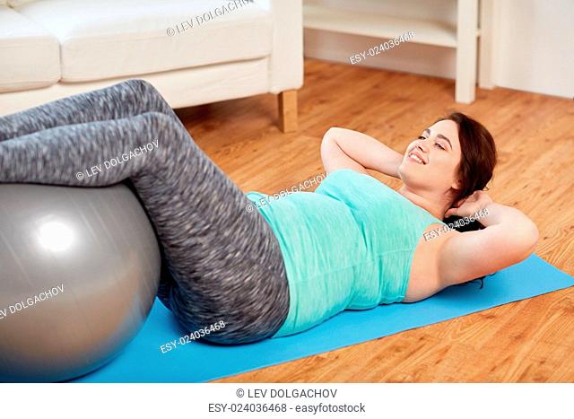 sport, people and healthy lifestyle concept - happy plus size young woman exercising with fitness ball on mat at home