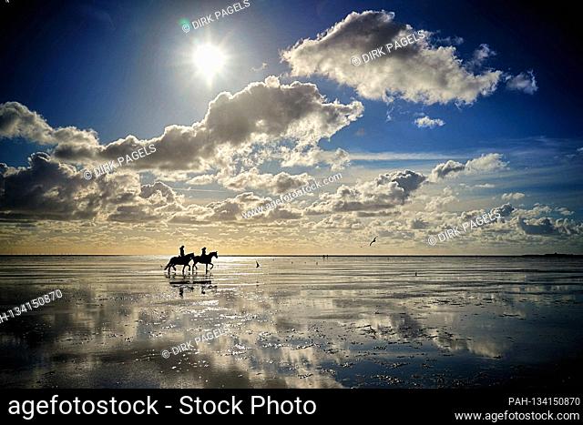 21.07.2020, Cuxhaven - Sahlenburg, the low tide on the North Sea attracts riders into the Wadden Sea who ride into the sunset