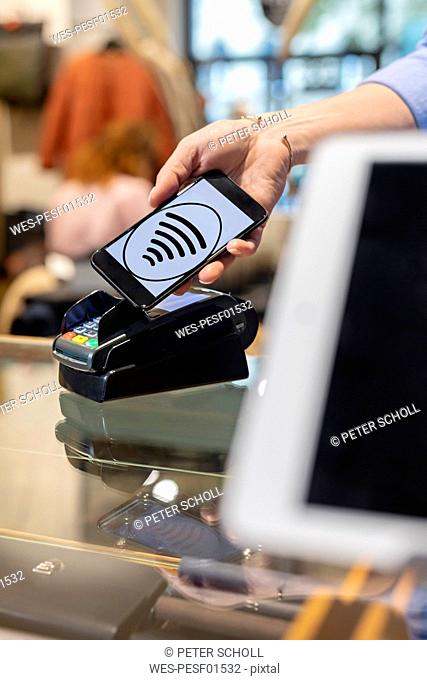 Customer paying contactless with smartphone in a fashion store