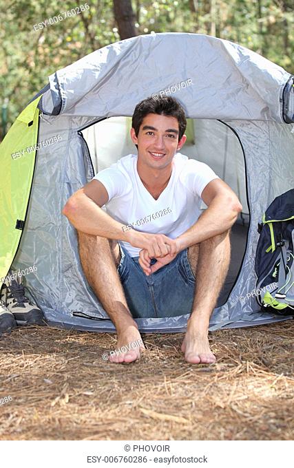 Teenage boy sitting in front of his tent on a sunny day