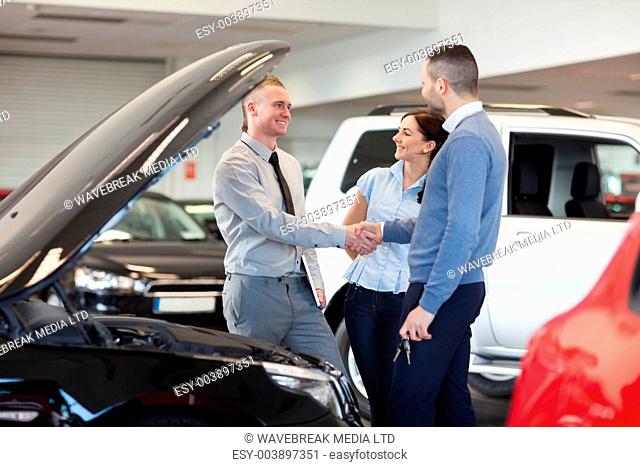 Man shaking hand of a car dealer in front of a car in a car shop
