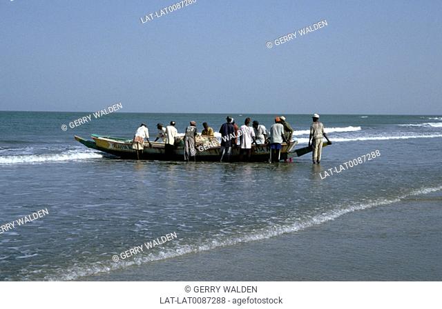 Grou p of men standing in shallow sea. Launching local wooden dugout boat