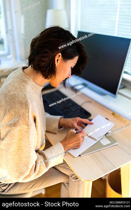 Businesswoman writing in note pad on table at home