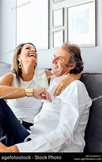 Woman with arm around man laughing on sofa in living room at home