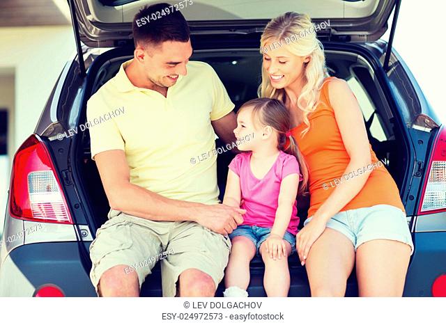 family , transport, leisure, road trip and people concept - happy man, woman and little girl sitting on trunk of hatchback car and talking outdoors
