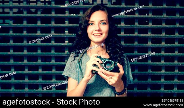 Pretty cool young woman with retro film camera, curly hair over city metal grid fence background