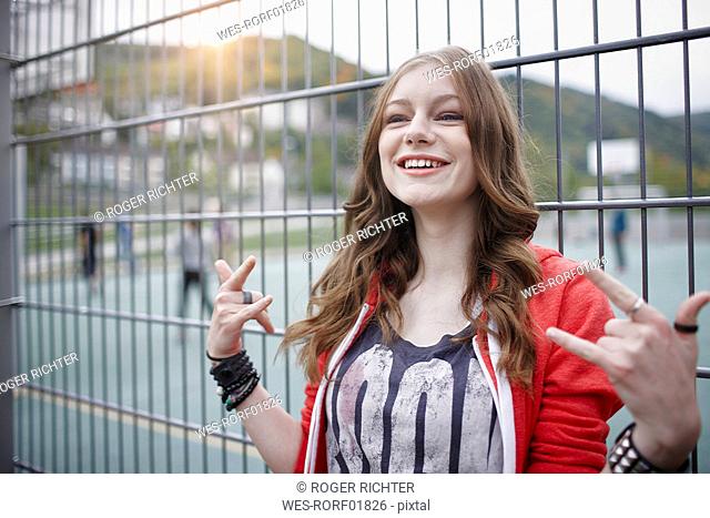 Portrait of a happy teenage girl gesturing at a fence at a sports field