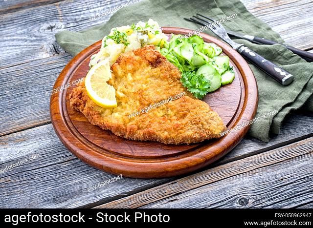 Traditional deep-fried schnitzel with potato and cucumber salad offered as closeu-up on a rustic wooden board with copy space