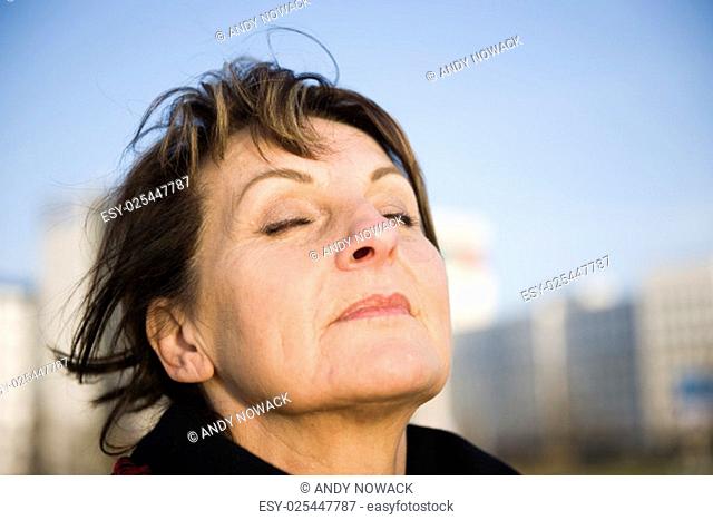 side head portrait of a mature woman in front blurred urban background with closed eyes a deep breath