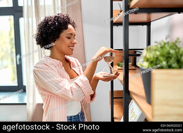 smiling woman with hourglass at shelf at home